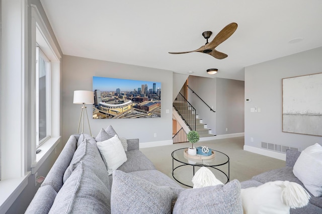 carpeted living room featuring stairs, baseboards, visible vents, and ceiling fan