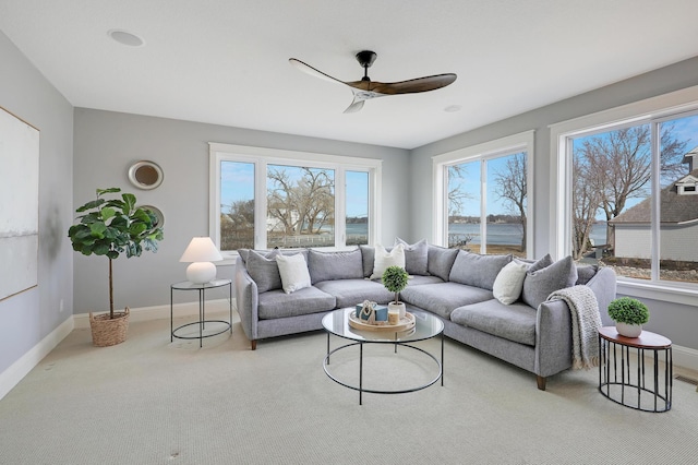 carpeted living area with baseboards and ceiling fan