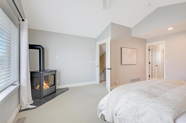 bedroom featuring baseboards, visible vents, lofted ceiling, a wood stove, and carpet flooring