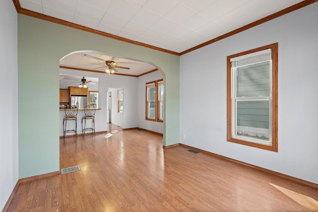 unfurnished living room with visible vents, light wood finished floors, arched walkways, ceiling fan, and crown molding