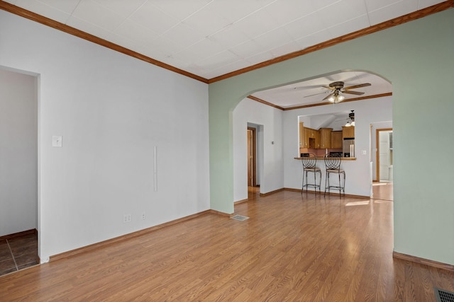 unfurnished living room featuring arched walkways, ornamental molding, a ceiling fan, and wood finished floors