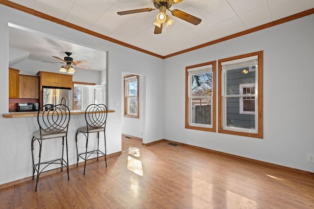 kitchen with light wood-type flooring, freestanding refrigerator, a breakfast bar area, black microwave, and ceiling fan