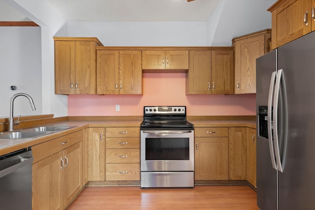 kitchen with a sink, stainless steel appliances, brown cabinets, and light wood-style flooring