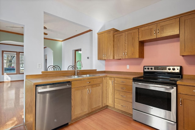 kitchen featuring light wood-style flooring, a sink, arched walkways, appliances with stainless steel finishes, and a peninsula