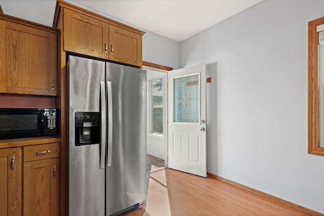 kitchen with baseboards, black microwave, light wood-type flooring, brown cabinetry, and stainless steel fridge