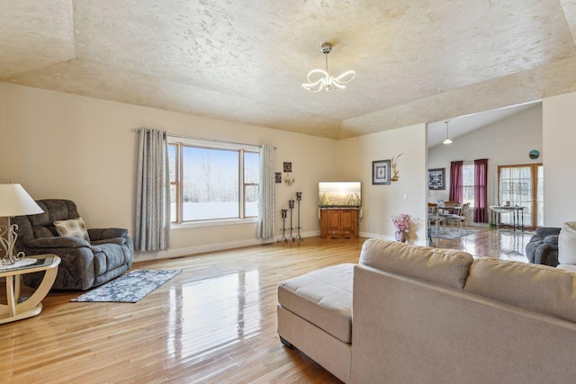 living room featuring light wood finished floors, baseboards, lofted ceiling, an inviting chandelier, and a textured ceiling