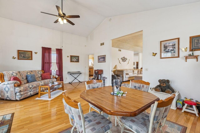 dining room featuring a ceiling fan, visible vents, light wood finished floors, and high vaulted ceiling