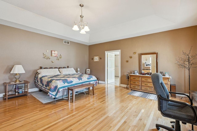 bedroom with baseboards, visible vents, a tray ceiling, light wood-style flooring, and a chandelier