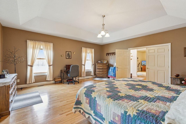 bedroom featuring visible vents, a raised ceiling, a notable chandelier, light wood finished floors, and baseboards