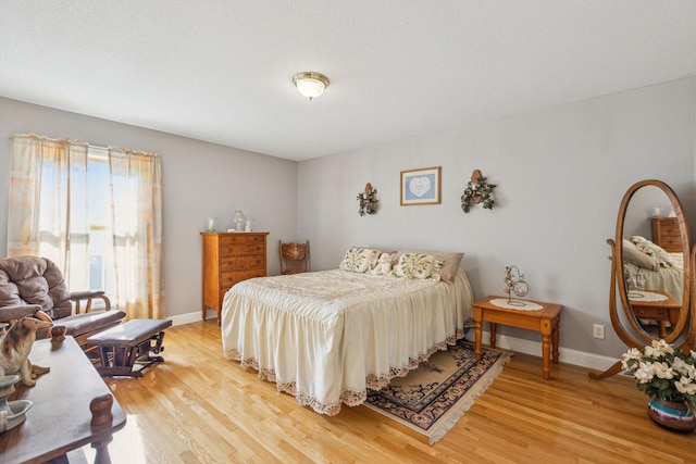 bedroom with light wood-type flooring, baseboards, and a textured ceiling