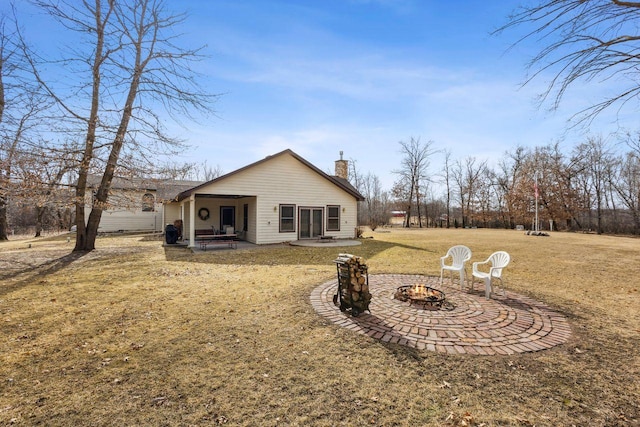 rear view of property featuring a patio, a fire pit, a lawn, and a chimney