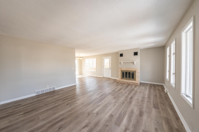 unfurnished living room with visible vents, baseboards, a chandelier, wood finished floors, and a textured ceiling