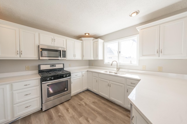 kitchen featuring white cabinetry, stainless steel appliances, light wood-style floors, and a sink