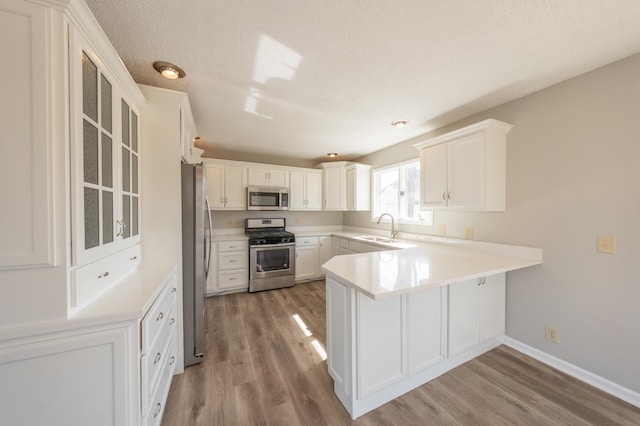 kitchen with wood finished floors, a peninsula, a sink, stainless steel appliances, and white cabinets