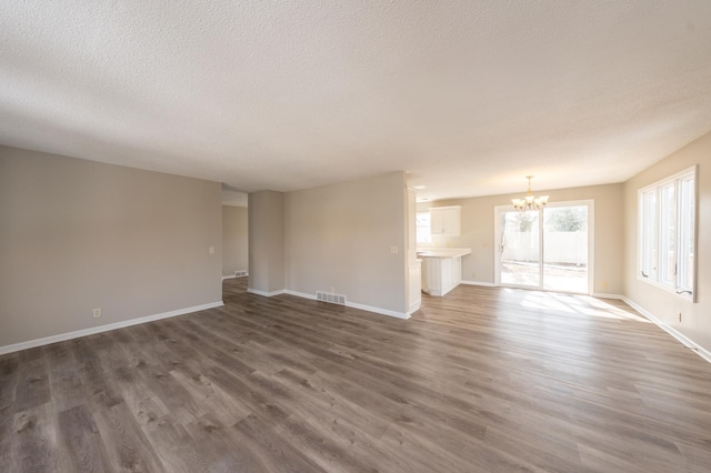 unfurnished living room with visible vents, baseboards, a chandelier, wood finished floors, and a textured ceiling