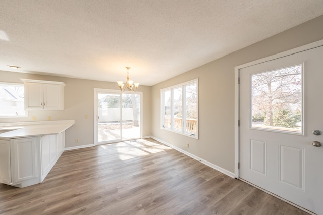 unfurnished dining area featuring baseboards, a textured ceiling, an inviting chandelier, and light wood finished floors