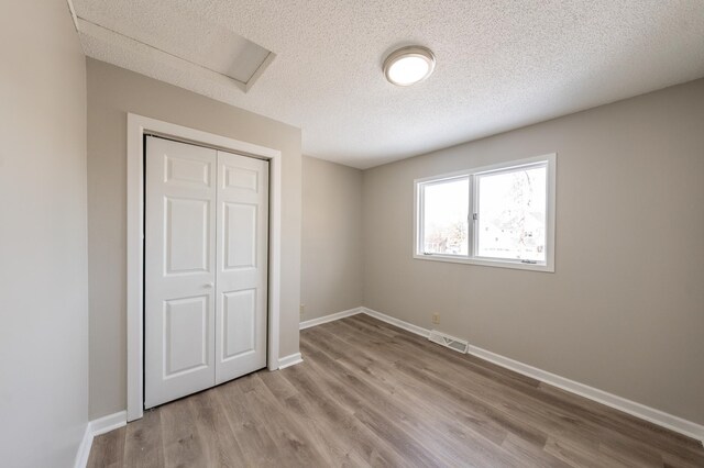 unfurnished bedroom with wood finished floors, visible vents, baseboards, attic access, and a closet