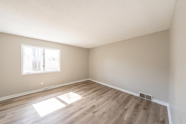 empty room with visible vents, a textured ceiling, baseboards, and wood finished floors