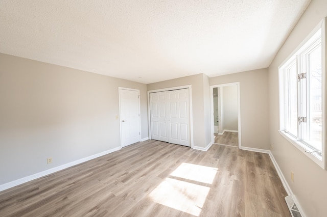 unfurnished bedroom with a textured ceiling, baseboards, a closet, and light wood-type flooring