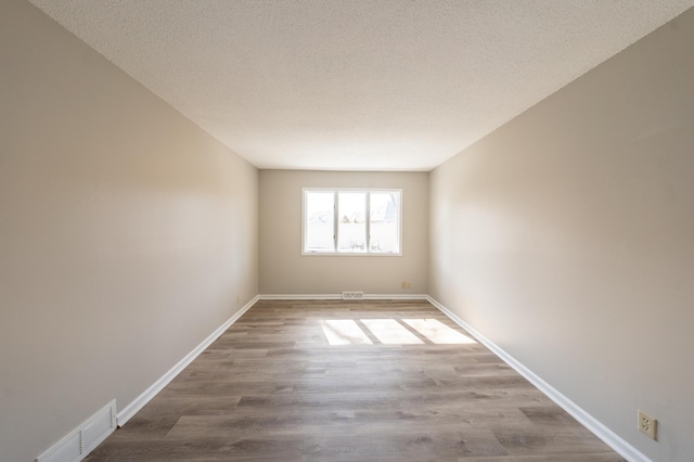 spare room featuring a textured ceiling, wood finished floors, visible vents, and baseboards