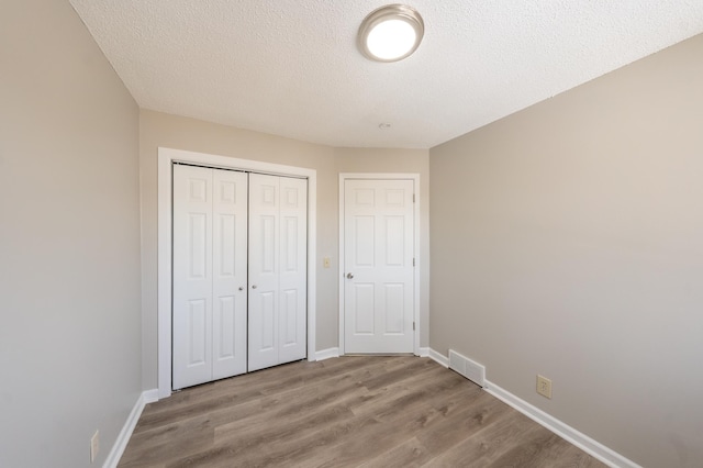 unfurnished bedroom featuring wood finished floors, visible vents, a closet, and baseboards