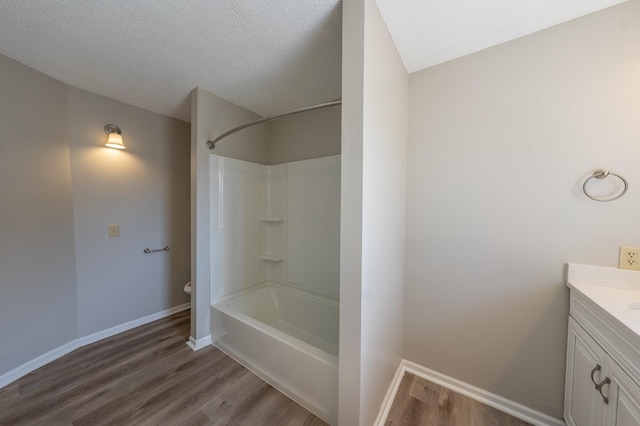 bathroom with vanity, wood finished floors, baseboards, a textured ceiling, and shower / bathtub combination