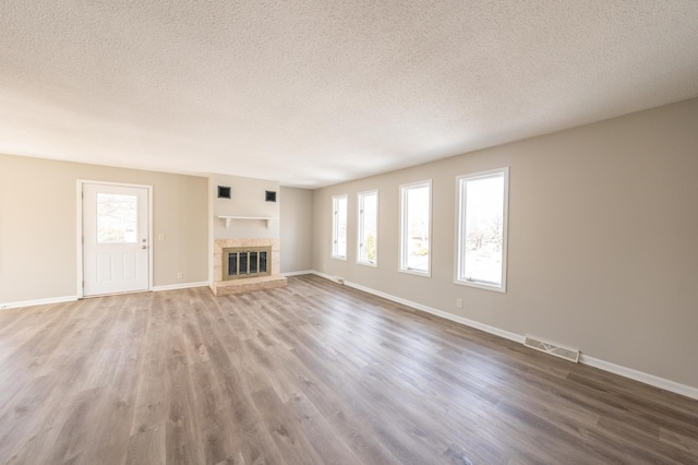 unfurnished living room with wood finished floors, visible vents, baseboards, a textured ceiling, and a glass covered fireplace