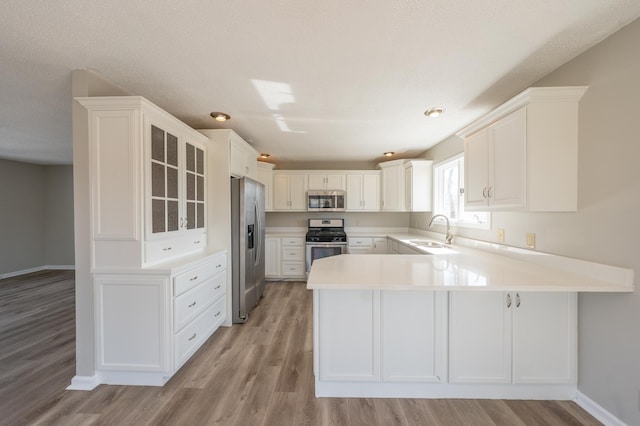 kitchen with a sink, a peninsula, white cabinets, and stainless steel appliances