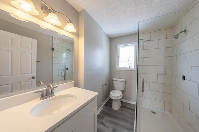 bathroom featuring toilet, a stall shower, wood finished floors, a textured ceiling, and vanity