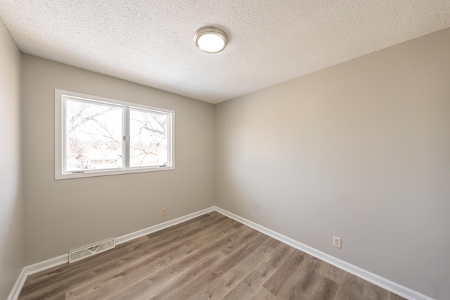 spare room featuring visible vents, a textured ceiling, baseboards, and wood finished floors