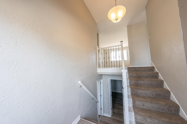 staircase with lofted ceiling, wood finished floors, and a textured wall