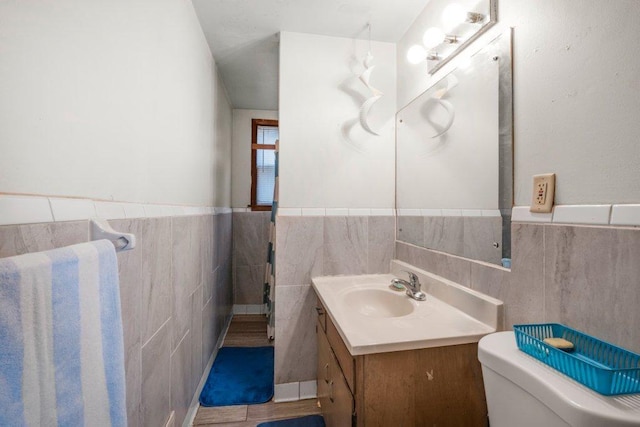 half bathroom featuring tile walls, wainscoting, toilet, and vanity