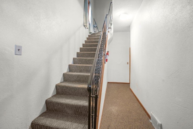 stairs featuring carpet flooring, visible vents, baseboards, and a textured wall