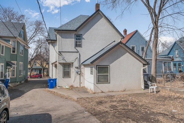 back of property with stucco siding, a chimney, and fence