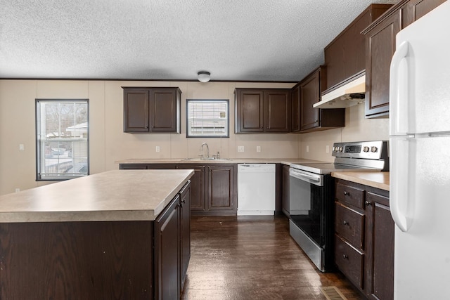 kitchen featuring under cabinet range hood, dark brown cabinetry, dark wood finished floors, white appliances, and a sink