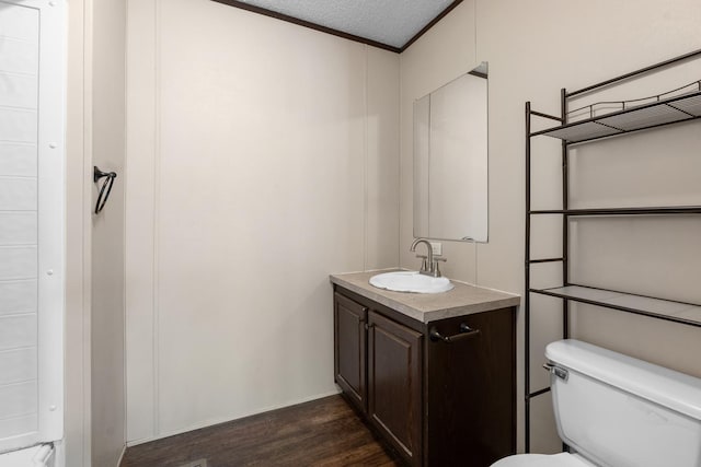 bathroom with toilet, ornamental molding, a textured ceiling, wood finished floors, and vanity