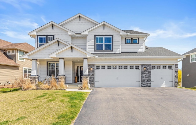 craftsman house featuring aphalt driveway, stone siding, roof with shingles, a porch, and a front lawn