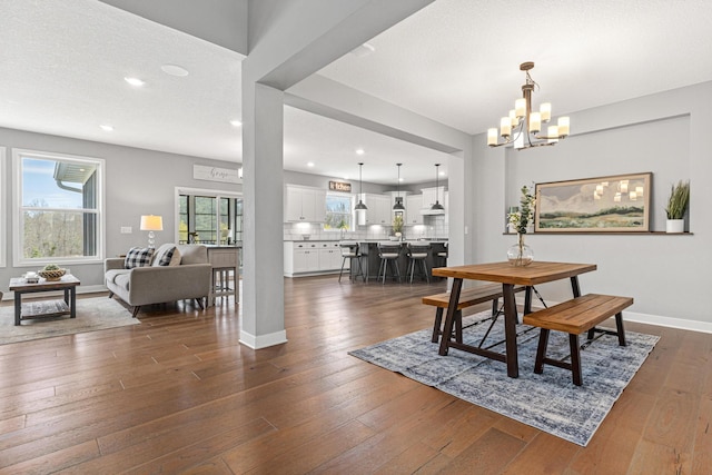 dining area with dark wood-type flooring, recessed lighting, an inviting chandelier, and baseboards