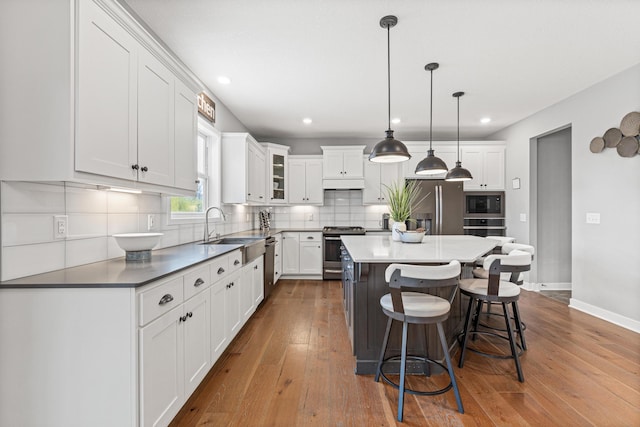 kitchen with tasteful backsplash, a breakfast bar, white cabinets, appliances with stainless steel finishes, and hardwood / wood-style flooring