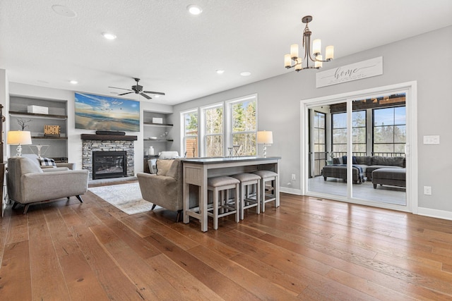 living area with a fireplace, hardwood / wood-style floors, baseboards, and ceiling fan with notable chandelier