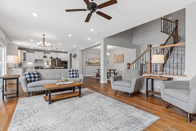 living area featuring recessed lighting, stairs, ceiling fan with notable chandelier, baseboards, and light wood-type flooring