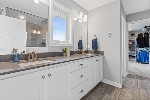 bathroom featuring baseboards, a tile shower, double vanity, and a sink
