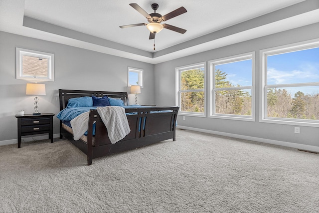 bedroom with ceiling fan, a raised ceiling, visible vents, light carpet, and baseboards