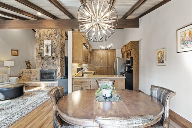 dining area featuring beamed ceiling, a notable chandelier, wood finished floors, and a fireplace