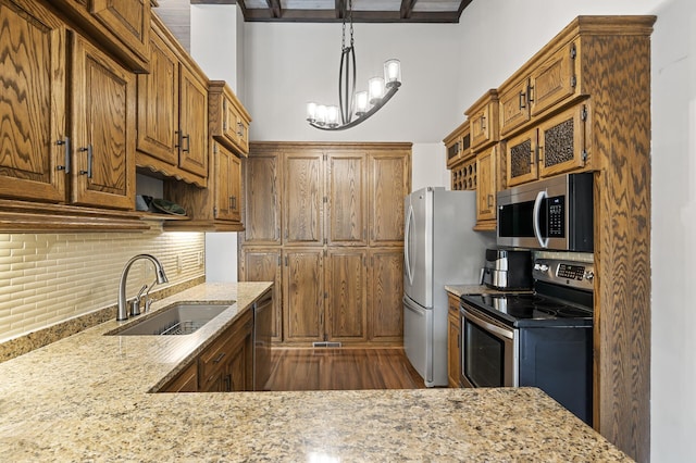 kitchen featuring backsplash, light stone counters, brown cabinets, stainless steel appliances, and a sink