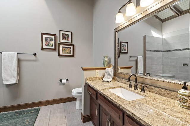 full bath with baseboards, toilet, vanity, and a tile shower