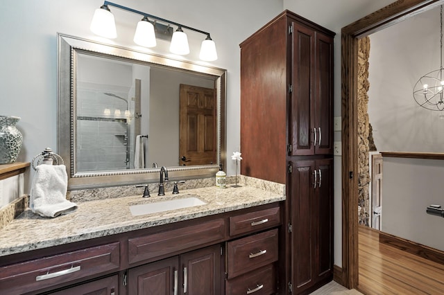 bathroom with a tile shower, vanity, an inviting chandelier, and wood finished floors