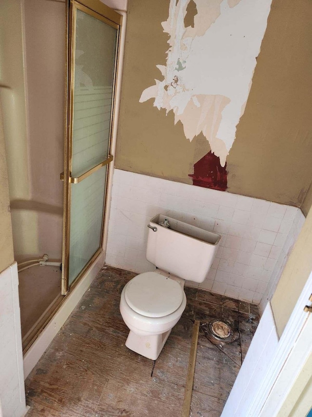 bathroom with a wainscoted wall, toilet, wood finished floors, tile walls, and a shower stall