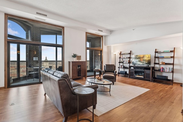 living area with visible vents, wood finished floors, a glass covered fireplace, a textured ceiling, and high vaulted ceiling