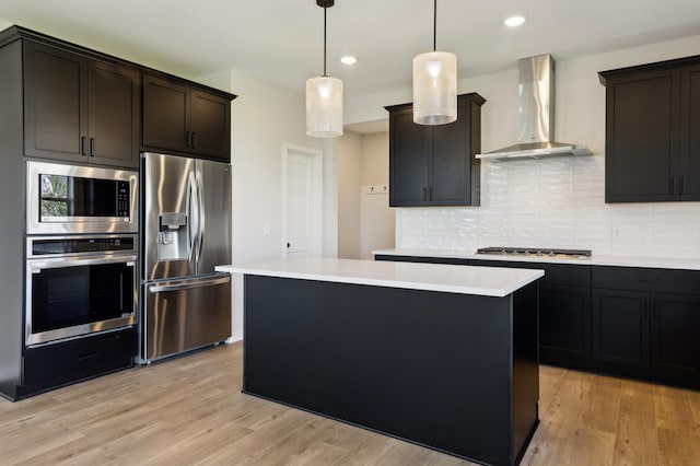 kitchen featuring a kitchen island, appliances with stainless steel finishes, wall chimney exhaust hood, and light countertops